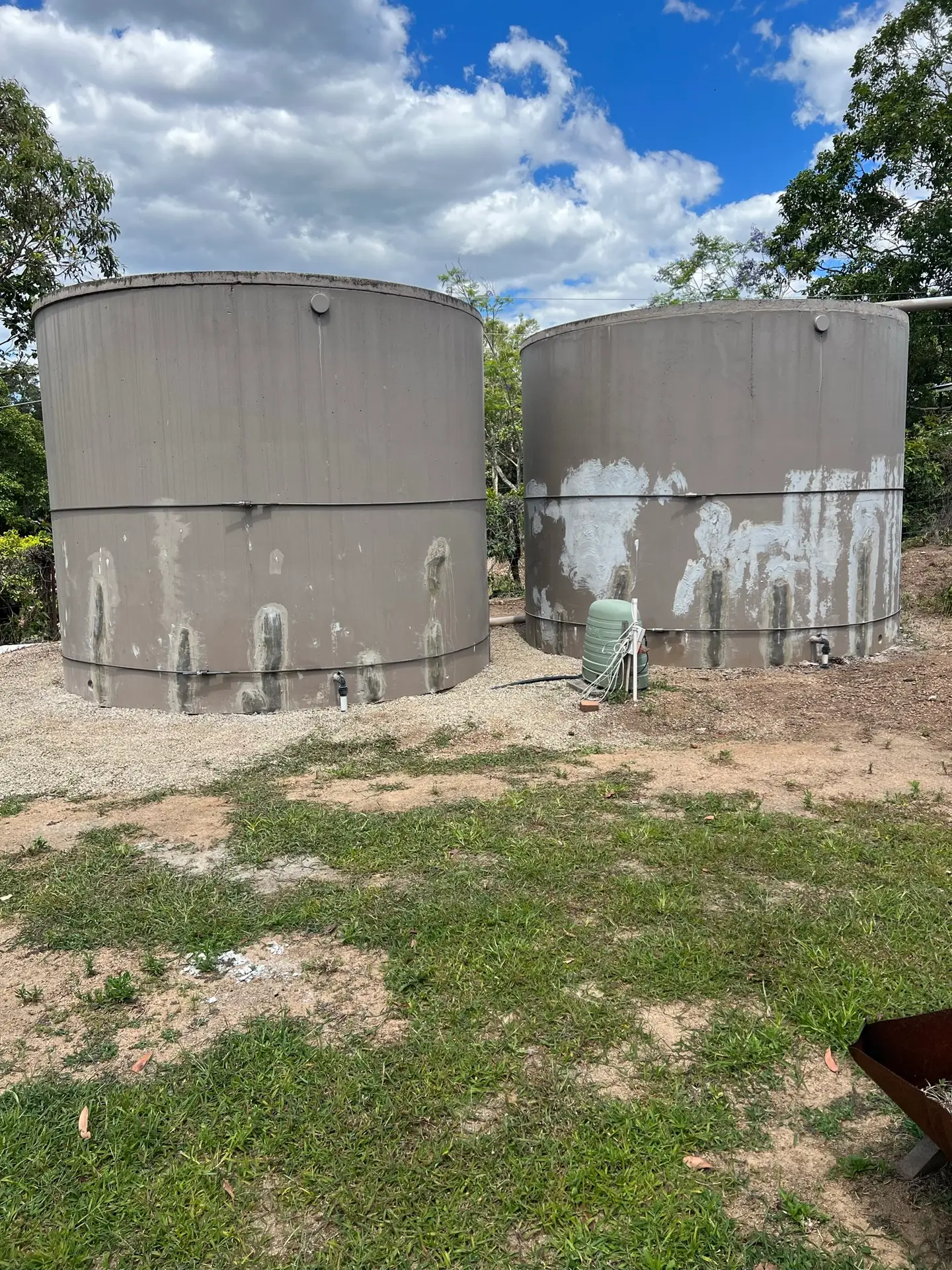 Two large outdoor concrete water storage tanks on a rural property showing exterior wear and maintenance needs.