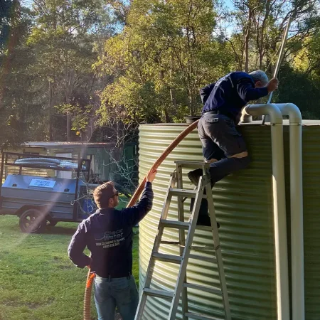 Clearwater Tank Services technicians cleaning a corrugated water tank using professional equipment on-site.